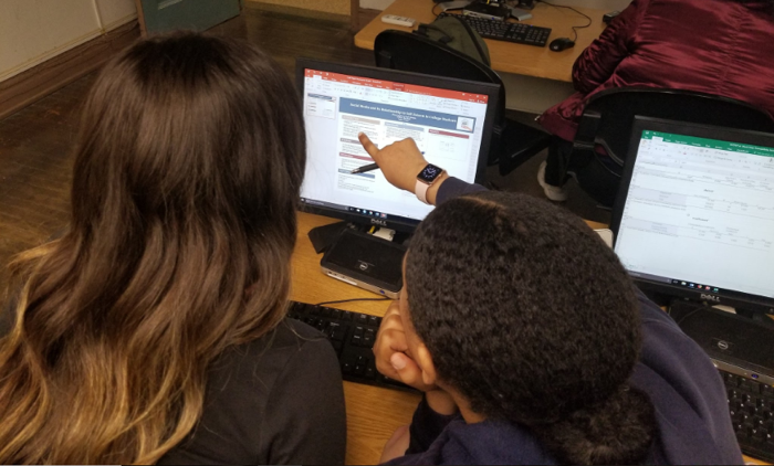 Two students are looking at a poster template on a computer screen. One is pointing at the screen.